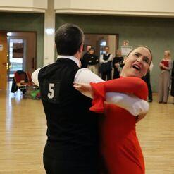 T&auml;nzerpaar in eleganten Kost&uuml;men auf einer Tanzfl&auml;che, Zuschauer im Hintergrund beobachten die Darbietung.