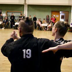 Tanzpaar in eleganter Kleidung w&auml;hrend einer Tanzauff&uuml;hrung, im Hintergrund Zuschauer an Tischen.