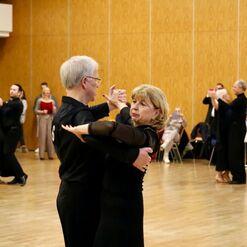 Tanzpaar in eleganter Kleidung tanzt im Vordergrund, w&auml;hrend andere Paare im Hintergrund ebenfalls tanzen.