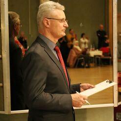 Ein Mann in einem Anzug steht seitlich vor einem Spiegel und h&auml;lt ein Notizblatt mit einem Stift in der Hand.