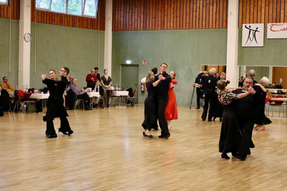 Tanzende Paare in eleganter Kleidung auf einer Tanzfl&auml;che, umgeben von Zuschauern an Tischen.