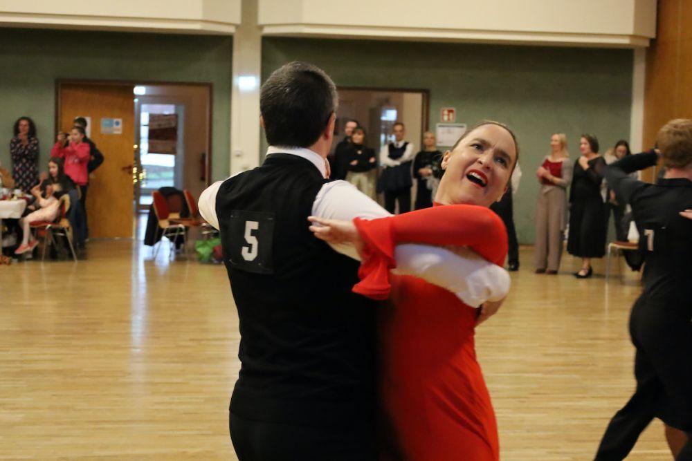 T&auml;nzerpaar in eleganten Kost&uuml;men auf einer Tanzfl&auml;che, Zuschauer im Hintergrund beobachten die Darbietung.