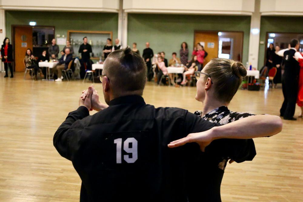 Tanzpaar in eleganter Kleidung w&auml;hrend einer Tanzauff&uuml;hrung, im Hintergrund Zuschauer an Tischen.