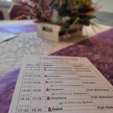 Tisch mit einem Programmheft für Tanzaufführungen und einer blühenden Dekoration im Hintergrund.