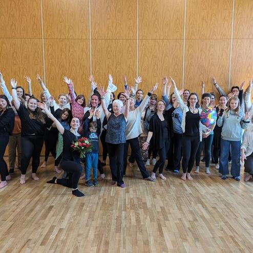 Gruppenfoto von 30 Personen, die in einem Raum mit Holzfußboden stehen und jubelnd die Hände heben.