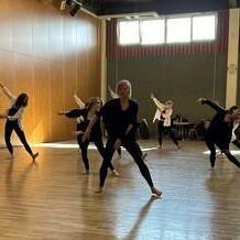Gruppe von Tänzerinnen in Schwarz führt eine choreografierte Aufführung in einem hellen Tanzraum auf.