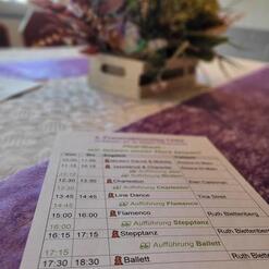Tisch mit einem Programmheft für Tanzaufführungen und einer blühenden Dekoration im Hintergrund.