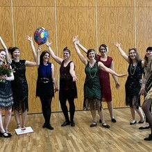 Gruppe von Frauen in 1920er-Jahre Kleidern feiert, hebt die H&auml;nde und h&auml;lt einen Luftballon in einem festlichen Raum.