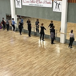 Gruppe von T&auml;nzern an einer Ballettstange, reflektiert in Spiegeln, in einem Tanzstudio mit Holzfu&szlig;boden.