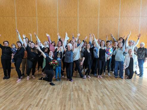 Gruppenfoto von 30 Personen, die in einem Raum mit Holzfußboden stehen und jubelnd die Hände heben.