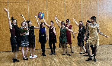 Gruppe von Frauen in 1920er-Jahre Kleidern feiert, hebt die H&auml;nde und h&auml;lt einen Luftballon in einem festlichen Raum.