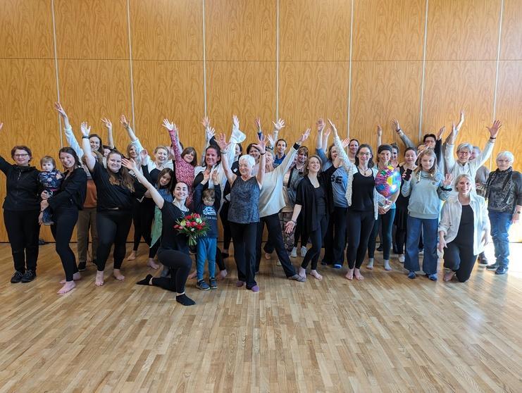 Gruppenfoto von 30 Personen, die in einem Raum mit Holzfußboden stehen und jubelnd die Hände heben.