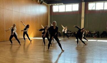 Gruppe von Tänzerinnen in Schwarz führt eine choreografierte Aufführung in einem hellen Tanzraum auf.
