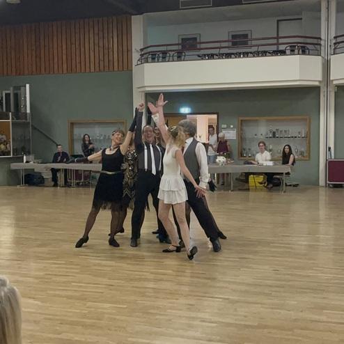 Tanzgruppe in eleganter Kleidung, die auf einer Holzfläche eine tänzerische Aufführung präsentiert.