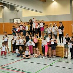 Gruppe von Kindern und Jugendlichen mit Urkunden in einer Sporthalle, einige stehen auf einer Holzkiste.