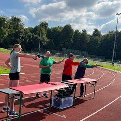 Vier Personen auf einer Sportanlage trainieren mit Luftgewehren während eines Schießübungsprogramms.