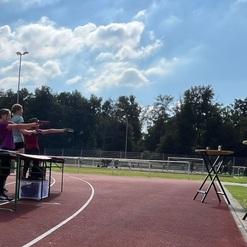 Drei Teilnehmer stehen an Tischen und zielen mit Sportluftdruckpistolen auf Zielscheiben im Freien.