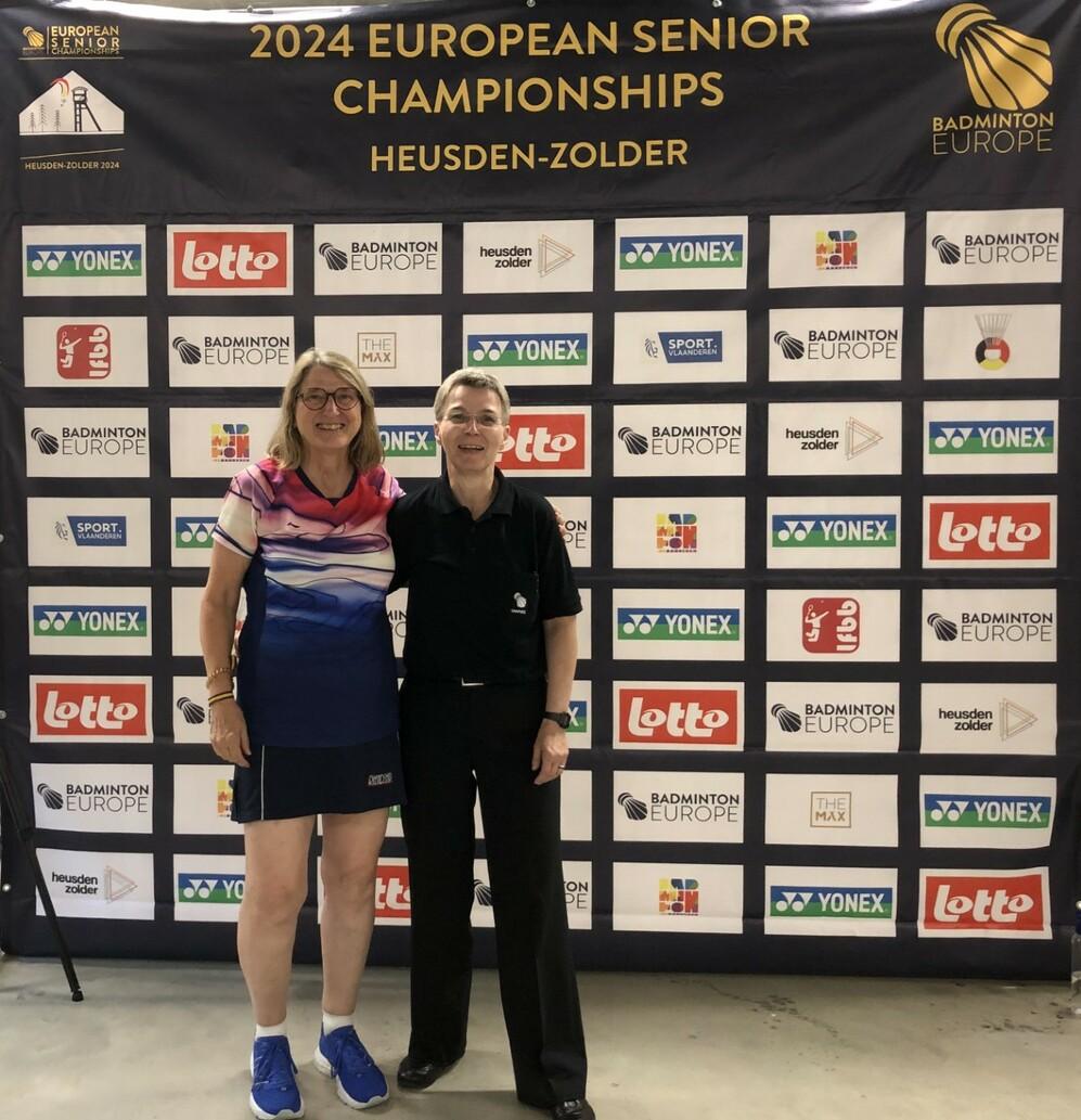 Zwei Frauen stehen vor einem Banner der 2024 European Senior Championships in Heusden-Zolder.