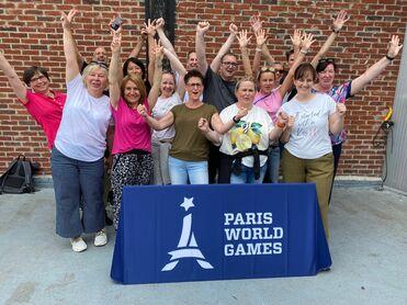 Gruppenfoto von Frauen und Männern, die vor einem Banner der Paris World Games mit erhobenen Händen jubeln.
