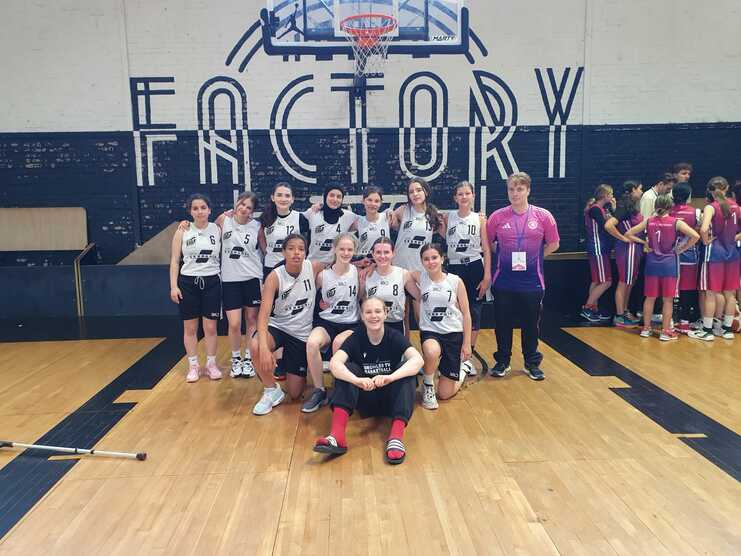 Teamfoto einer Basketballmannschaft in einheitlichen Trikots, vor einer Wand mit dem Schriftzug „FACTORY“.