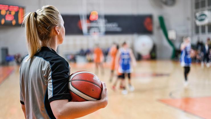 Schiedsrichterin mit Basketball beobachtet ein Spiel auf dem Court in einer Sporthalle.