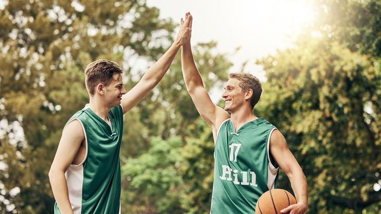 Zwei Basketballspieler in grünen Trikots geben sich einen High-Five, während einer einen Basketball hält.