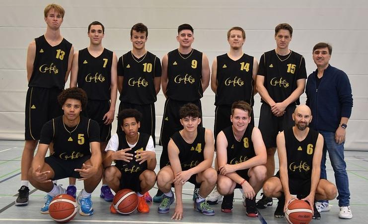 Gruppenfoto von zehn Basketballspielern in schwarzen Trikots mit B&auml;llen, auf einem Sportfeld in einer Halle.