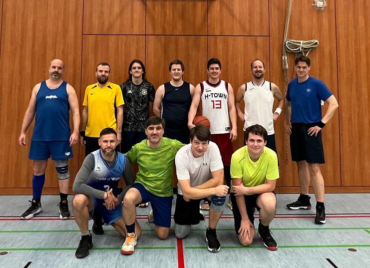 Gruppe von zehn Männern in Sportbekleidung, die gemeinschaftlich in einer Sporthalle posieren, einige mit Basketball.