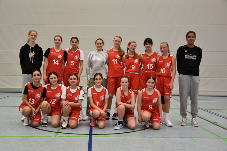 Basketballteam bestehend aus 15 M&auml;dchen in roten Trikots, stehend und sitzend in einer Sporthalle.