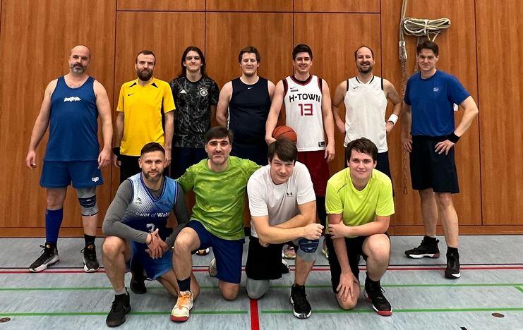 Gruppe von zehn M&auml;nnern in Sportbekleidung, die gemeinschaftlich in einer Sporthalle posieren, einige mit Basketball.