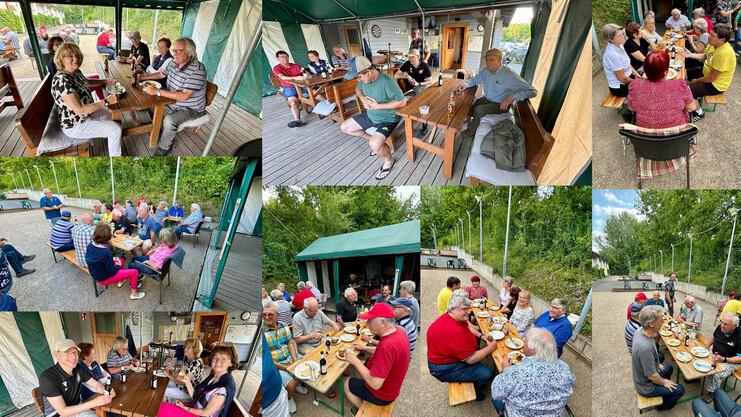 Gruppenszene mit mehreren Menschen beim Essen und Trinken unter einem Pavillon, umgeben von Bäumen und einer Sportanlage.