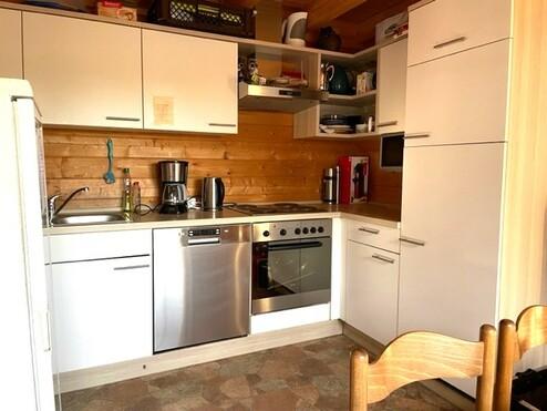 Moderne Küche mit weißen Schränken, Edelstahlgeräten, Holzverkleidung und einem kleinen Esstisch im Vordergrund.