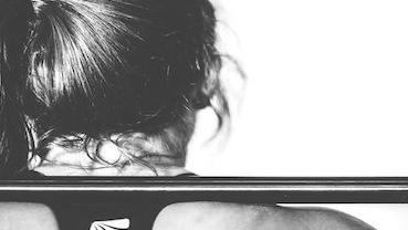 Nahaufnahme einer Person von hinten, die eine Langhantel auf den Schultern hält, bereit für ein Training.