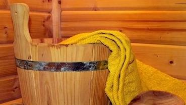 Holzbadewanne mit gelbem Handtuch und Holzlöffel vor einer vertäfelten Wand aus hellen Holzpaneelen.
