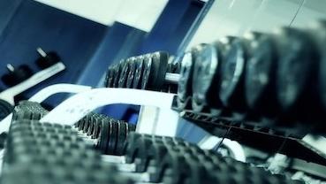 Nahaufnahme einer Hantelbank mit gestapelten Hanteln und einem Spiegel im Hintergrund in einem Fitnessstudio.