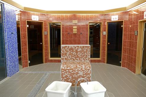 Innenansicht eines Saunabereichs mit bunten Fliesen, einem mosaikverzierten Sitzplatz und zwei Sanitärschalen.