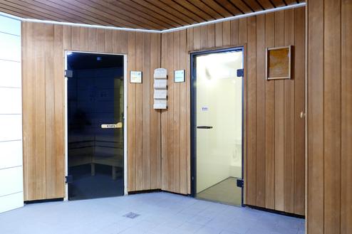 Eingangsbereich einer Sauna mit zwei Türen, eine in Holzoptik und die andere in durchsichtigem Glas.