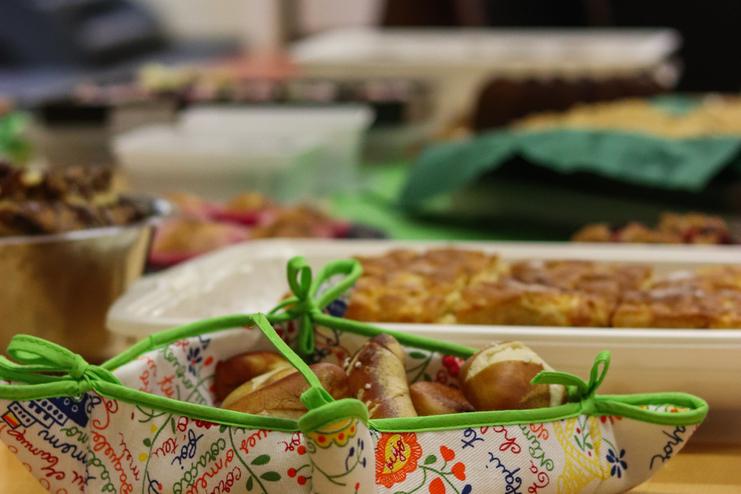 Blick auf einen Tisch mit verschiedenen Speisen, darunter Brezeln in einer bunten Schale und andere Gerichte.
