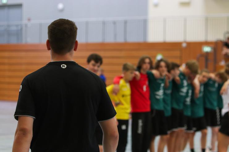 Trainer steht vor einer Reihe von Jugendlichen in Sportkleidung, die sich zur Mannschaftsbesprechung aufstellen.