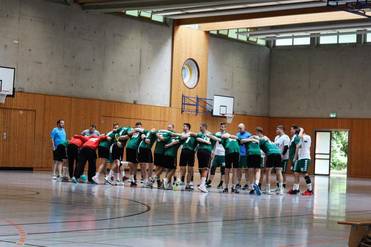 Gruppierung von Handballspielern in sportlichen Trikots, die sich in einer Sporthalle warmmachen.
