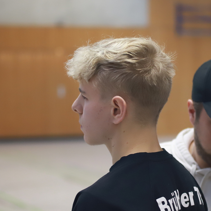 Zwei junge Männer stehen in einer Sporthalle, einer trägt ein schwarzes Shirt mit der Aufschrift "Brüder 1".