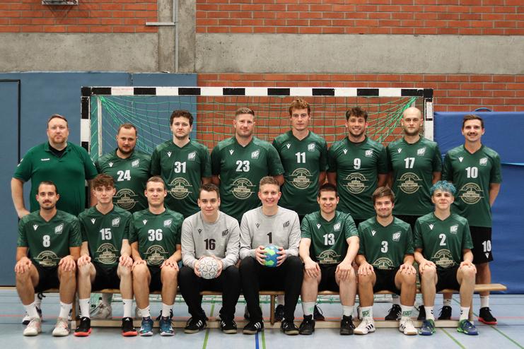 Mannschaftsbild einer Handballmannschaft in grünen Trikots, sitzend und stehend vor einem Tor.