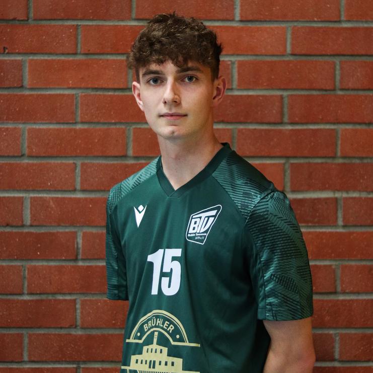 Junger Mann in einem grünen Sporttrikot mit der Nummer 15, vor einer rotgemauerten Wand.