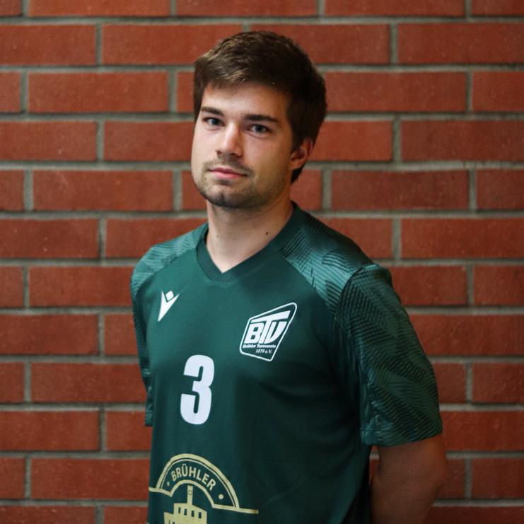 Junger Mann in einem grünen Sporttrikot mit der Nummer 3 steht vor einer Ziegelwand.