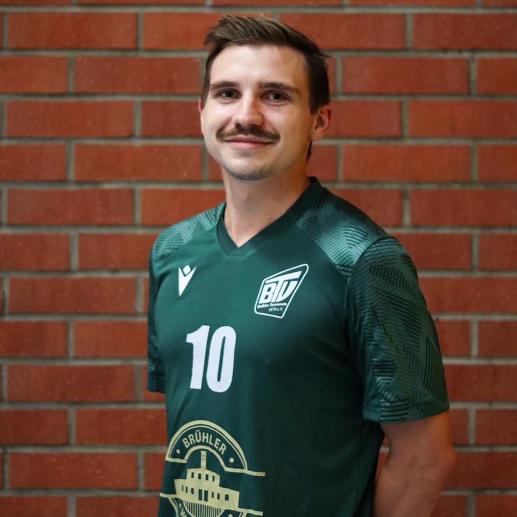 Porträt eines Mannes mit Schnurrbart, der ein grünes Trikot mit der Nummer 10 vor einer Ziegelwand trägt.