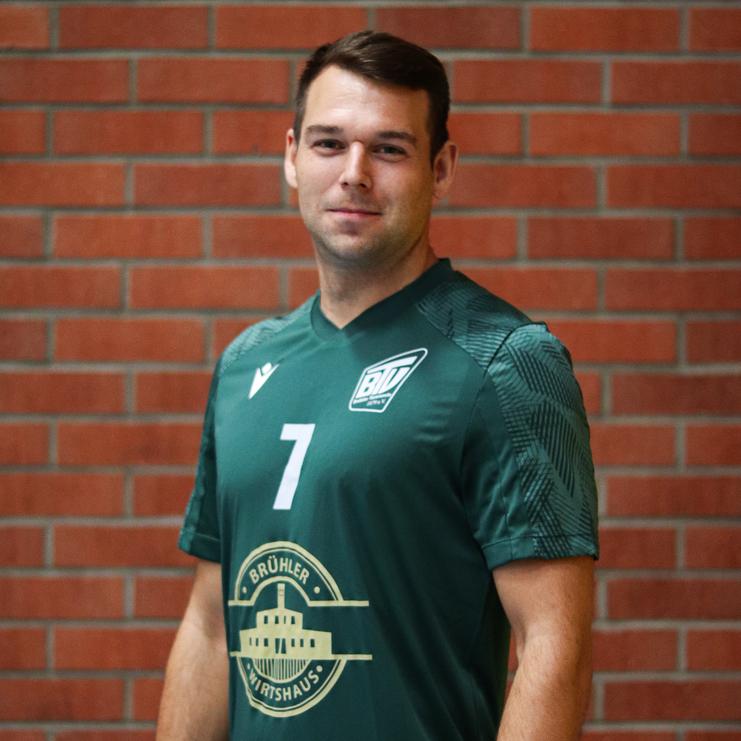 Porträt eines Mannes in grünem Sporttrikot mit der Nummer 7, vor einer Backsteinwand stehend.