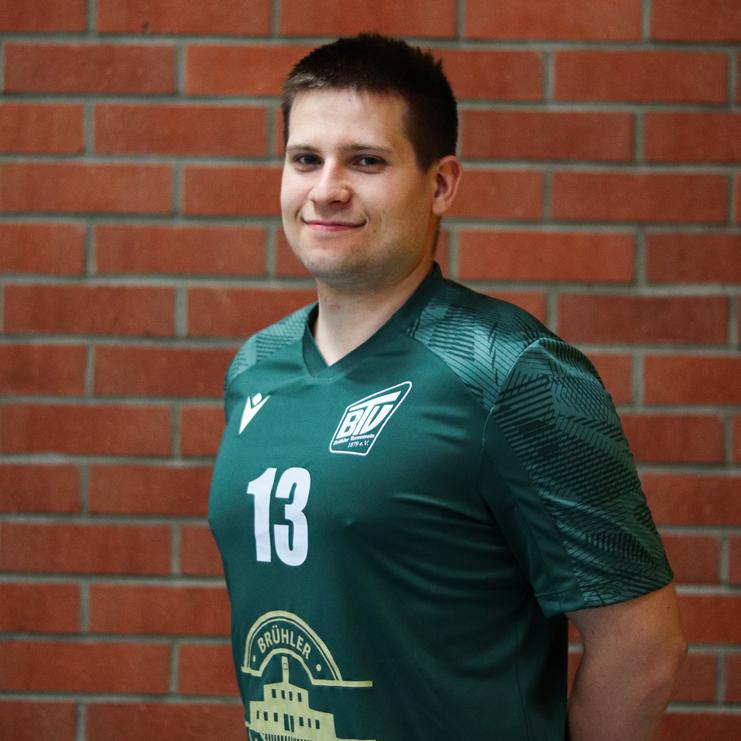 Mann in grünem Sporttrikot mit der Nummer 13 posiert vor einer Backsteinwand.