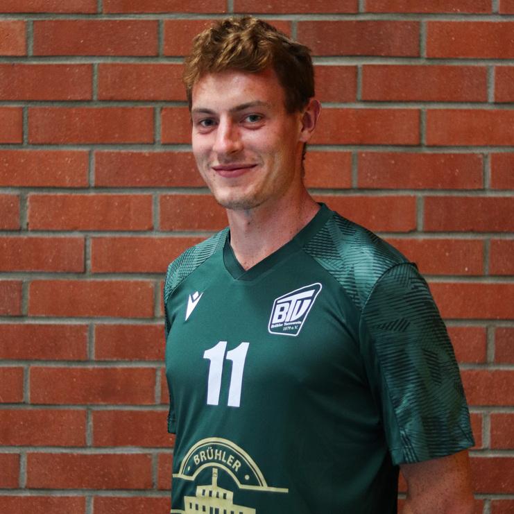 Lächelnder junger Mann in einem grünen Sporttrikot mit der Nummer 11 steht vor einer Backsteinwand.