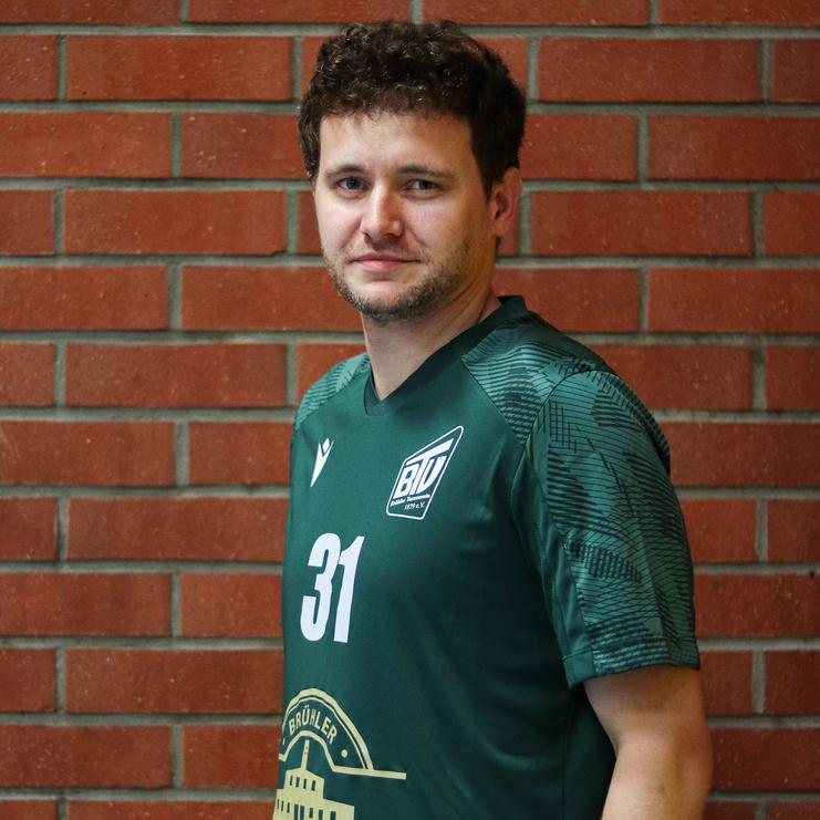 Portrait eines Mannes in einem grünen Sporttrikot mit der Nummer 31, stehend vor einer roten Ziegelwand.