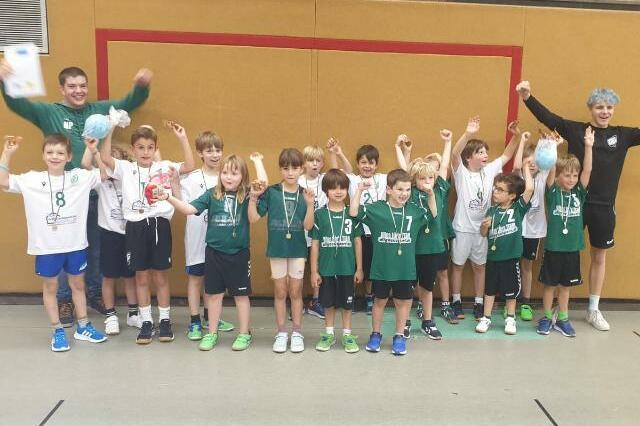 Gruppe von Jugendlichen in Sportkleidung mit Medaillen, die jubeln und feiern in einer Sporthalle.